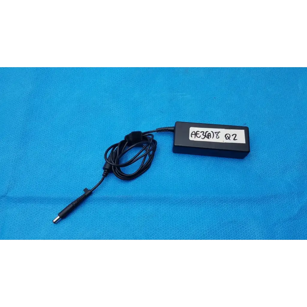 Black rectangular delta electronics adp-90ce laptop charger with coiled cable and handwritten label on surface