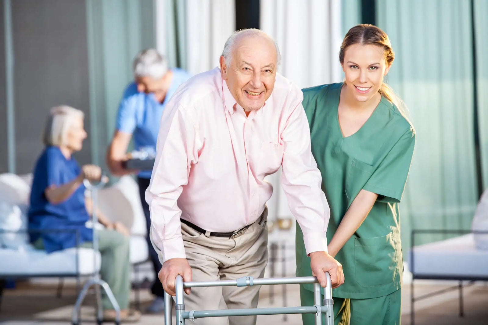 Elderly man using a silver-framed walker with a smiling caregiver beside him