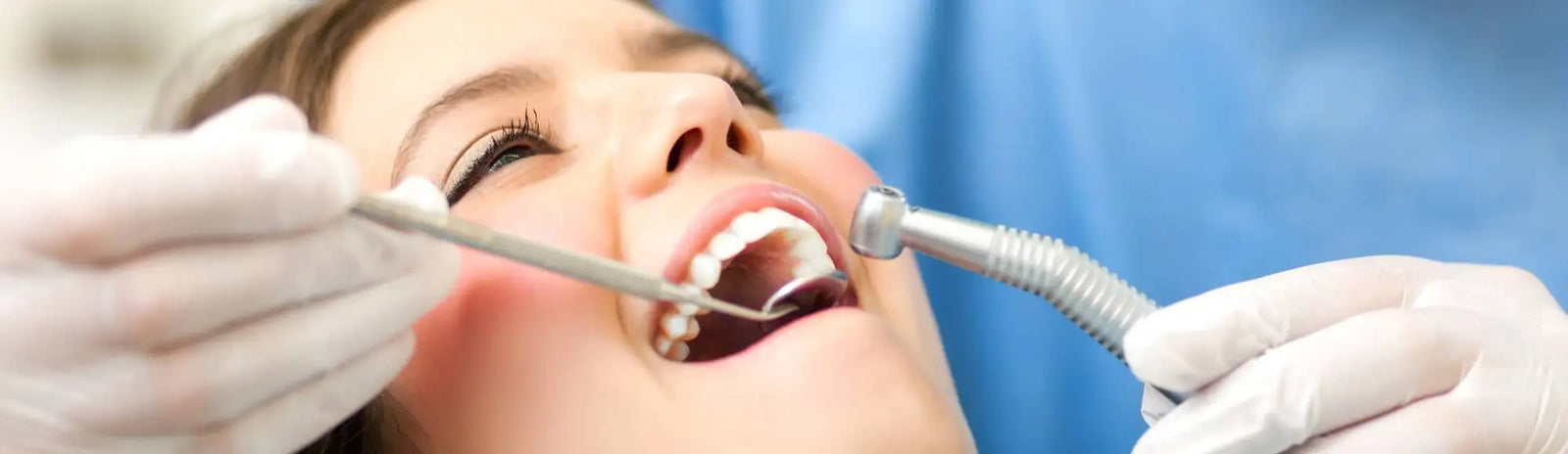 Silver dental handpiece with a flexible metallic hose and a curved tip, held by gloved hands during an oral examination.