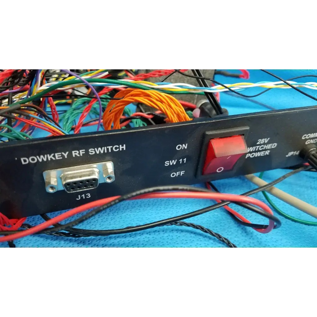 Black dowkey rf switch with red power toggle and silver db9 port surrounded by wiring on 19-inch rackmount control panel interface