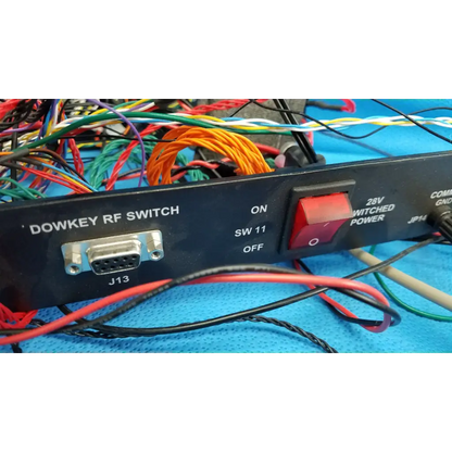 Black dowkey rf switch with red power toggle and silver db9 port surrounded by wiring on 19-inch rackmount control panel interface