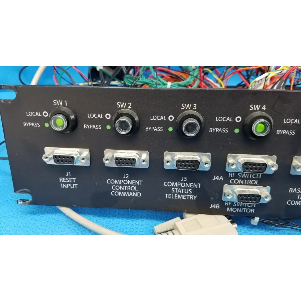 Black 19-inch rackmount control panel interface with four green-lit rotary switches and silver db9 serial ports