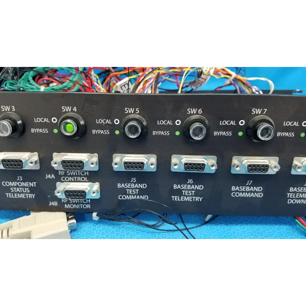Black 19-inch rackmount control panel interface with multiple labeled ports, switches, and green indicator lights on back side