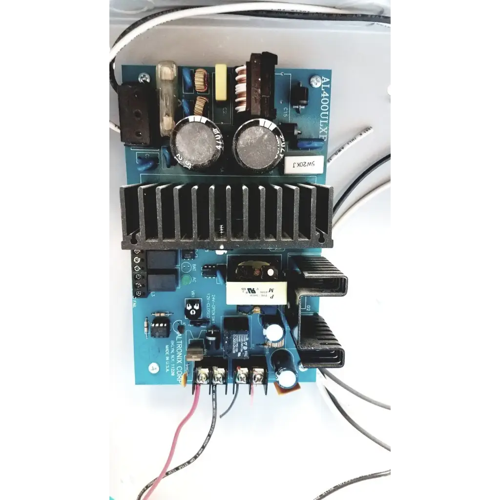 Blue circuit board with black heat sinks and silver capacitors in altronix al400ulx power supply charger 12vdc or 24vdc