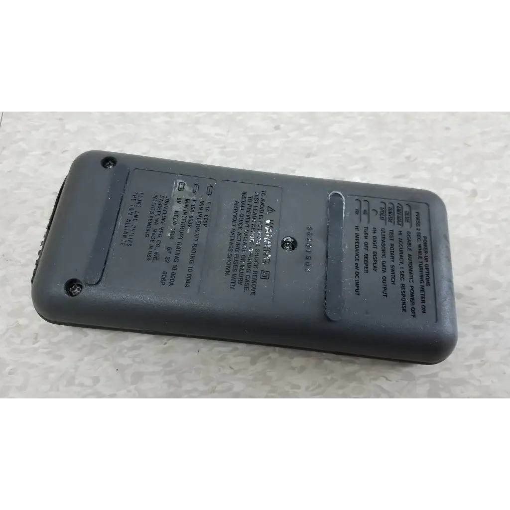 Back of gray plastic fluke 87 true rms digital handheld multimeter with printed specs and small circular button
