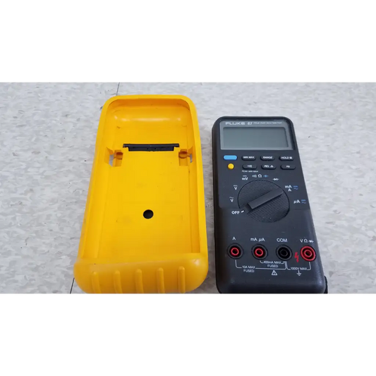 Black fluke 87 true rms digital handheld multimeter with red and black test leads next to yellow protective case