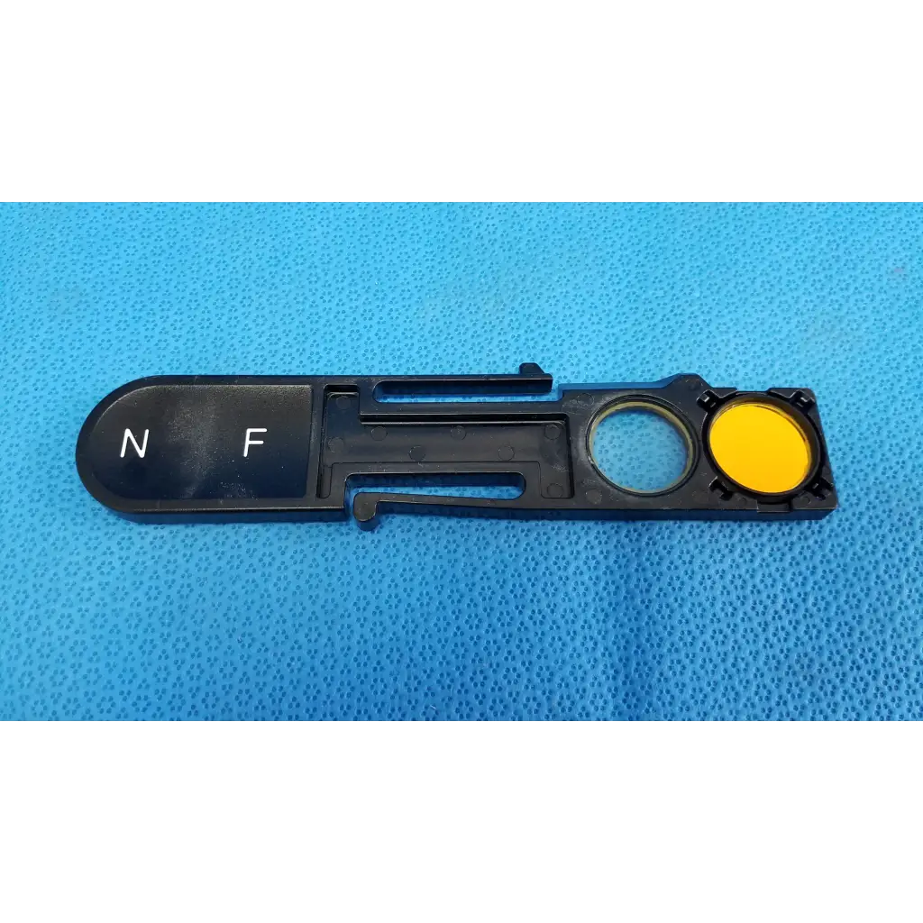 Black plastic optical filter slider with yellow circular component and white n f markings for topcon fundus retinal camera