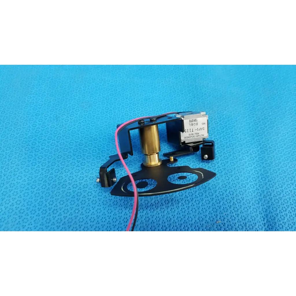 Black and brass rotary solenoid aperture diaphragm labeled globel 1908 mounted on black plastic base for topcon camera