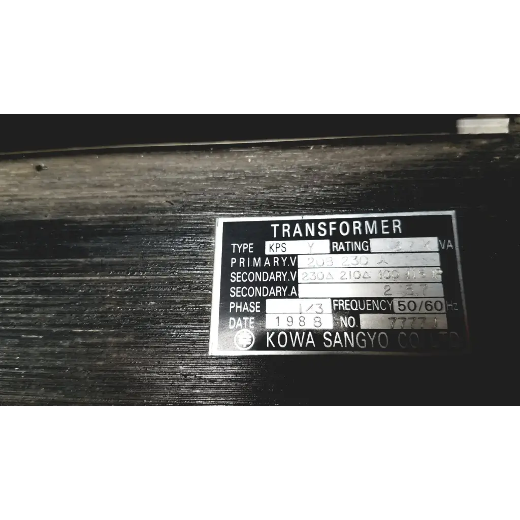 Silver metallic label on a dark surface showing technical specifications for kowa sangyo power transformers reuse medical product