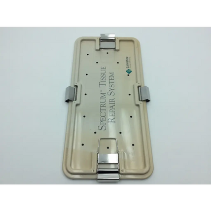 Beige plastic surgical plate with silver metal clamps engraved with spectrum tissue repair system by linvatec spectrum