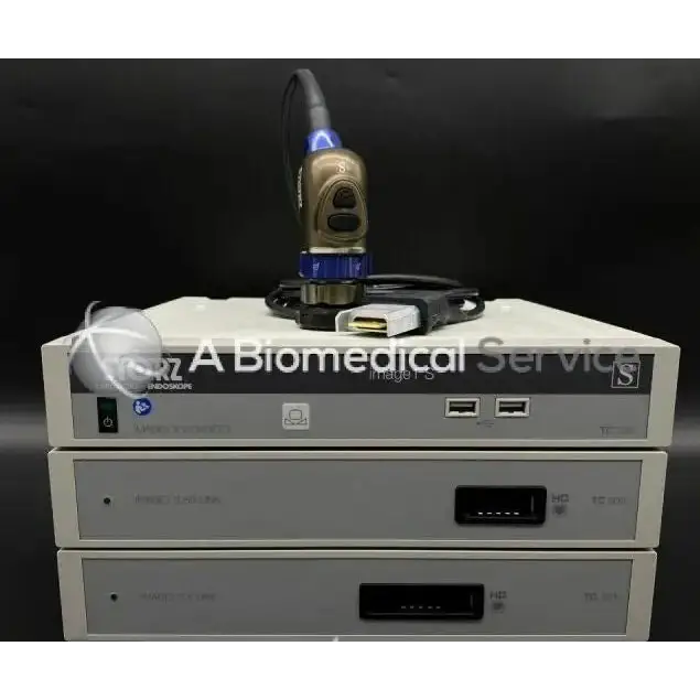 Gold-colored endoscope with blue illuminated tip resting on white medical imaging consoles in storz image1 s 3d system