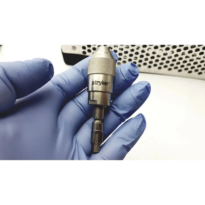 Metallic stryker system 7 large bone battery powered drill chuck with textured grip held in blue surgical gloves