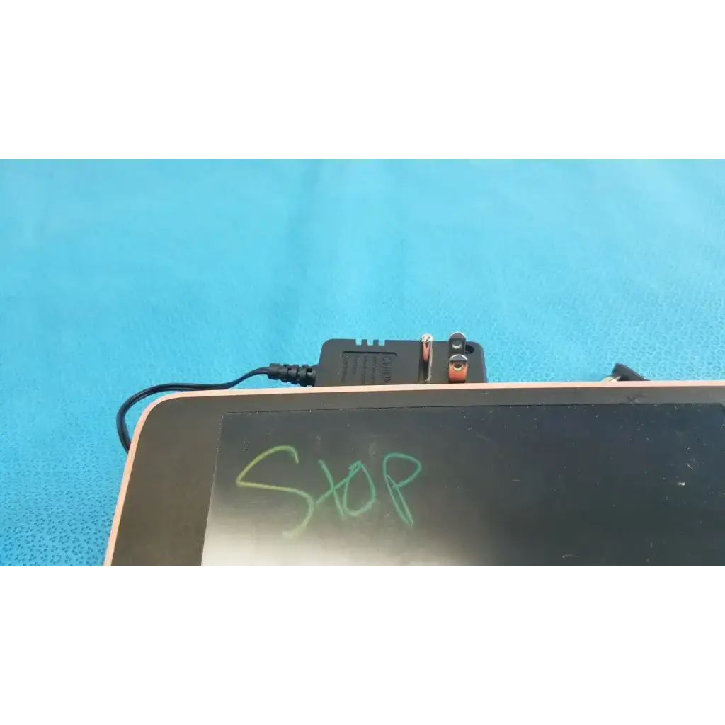 Black rectangular welch allyn transformer adapter power supply with orange and silver terminals connected to tablet edge