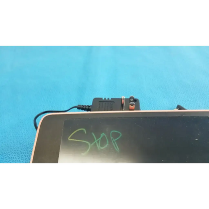 Black rectangular welch allyn transformer adapter power supply with orange and silver terminals connected to tablet edge