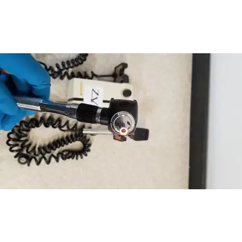 Black Welch Allyn otoscope with circular lens housing and coiled metal cable for wall transformer reuse medical use