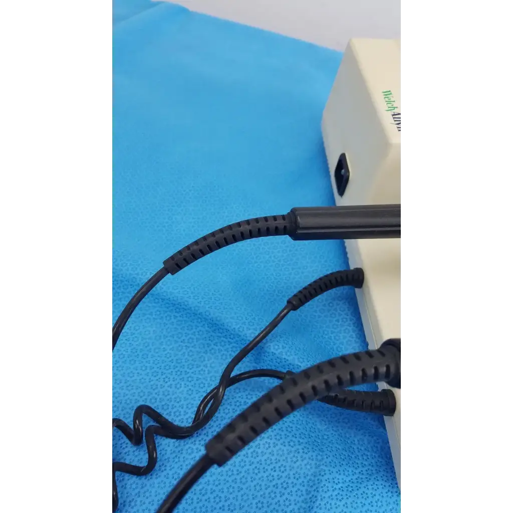 Black coiled cables with ribbed protective sleeves connected to the back of a beige welch allyn 767 series wall transformer