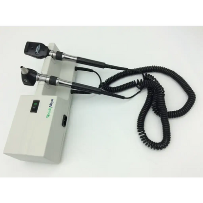 Medical-grade Welch Allyn otoscope with black and silver handles, coiled cable, and beige Welch Allyn 767 Wall Transformer 25020A base unit