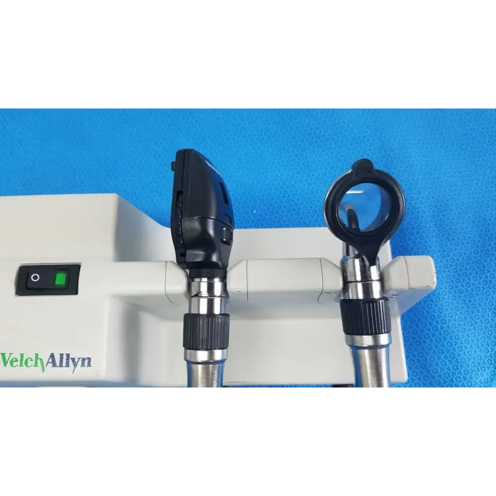 Black and silver welch allyn otoscope with circular lens and angled head mounted on white wall transformer base unit for reuse medical use