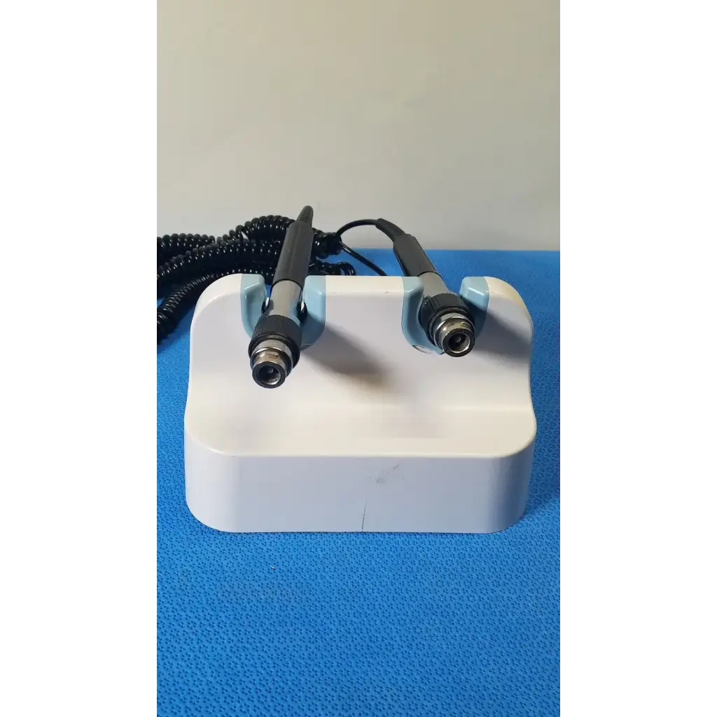 White plastic stand holding two black and silver handheld welch allyn wall transformer medical devices with coiled cords