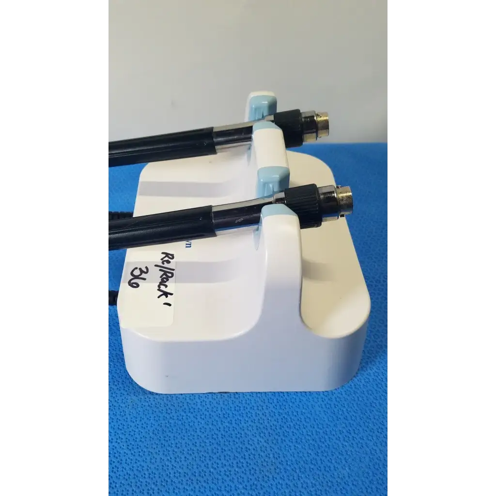 White plastic stand holding two black welch allyn medical-grade endoscopes with metallic connectors and coiled cords on wall transformer