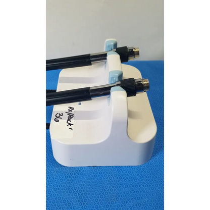 White plastic stand holding two black welch allyn medical-grade endoscopes with metallic connectors and coiled cords on wall transformer
