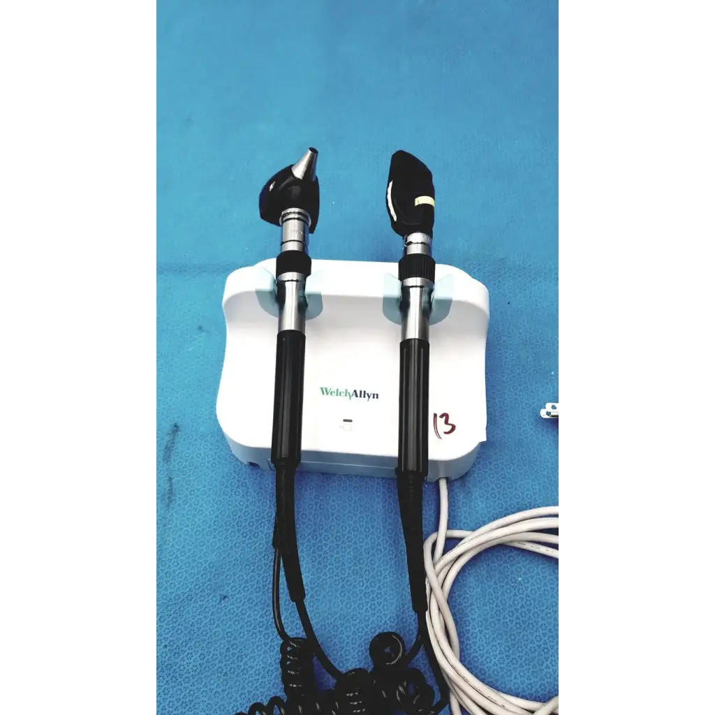 Welch allyn wall transformer with black and silver otoscope handles mounted on a white charging base for reuse medical use