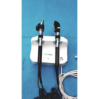 Welch allyn wall transformer with black and silver otoscope handles mounted on a white charging base for reuse medical use