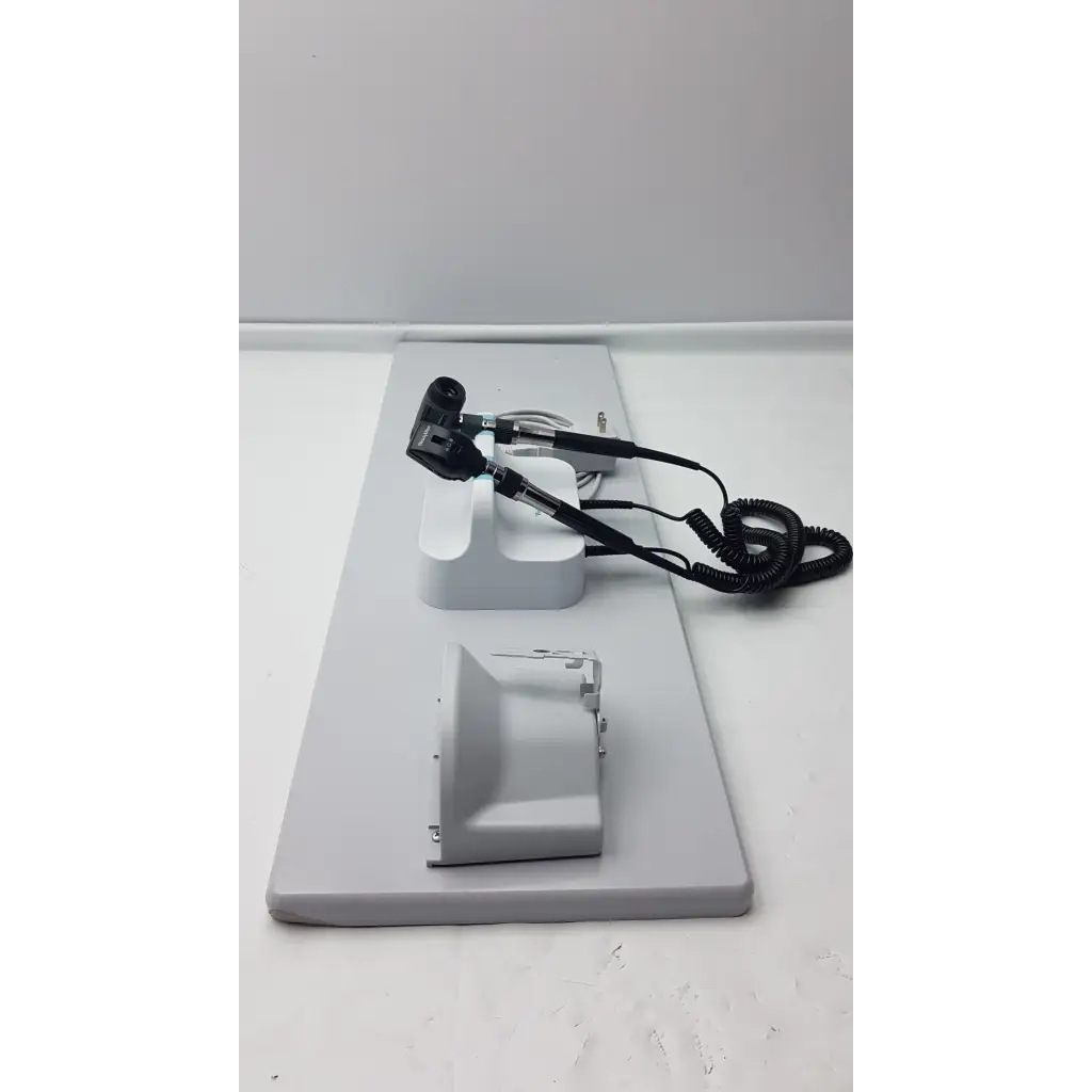 Black and silver Welch Allyn wall transformer otoscope with coiled cord on white stand in diagnostic set base