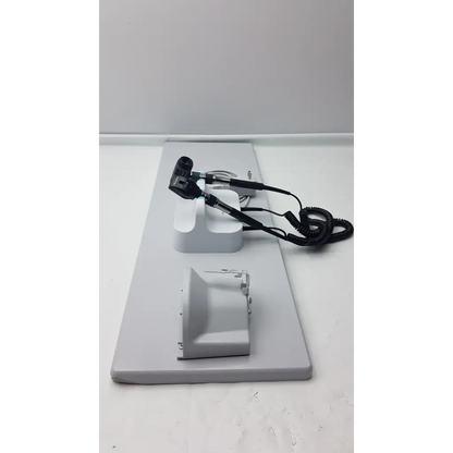 Black and silver Welch Allyn wall transformer otoscope with coiled cord on white stand in diagnostic set base