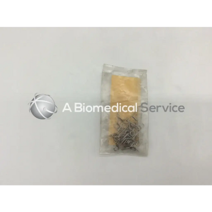 A clear plastic bag containing multiple metallic howmedica orthopedic fixation stop clips with a yellow paper insert