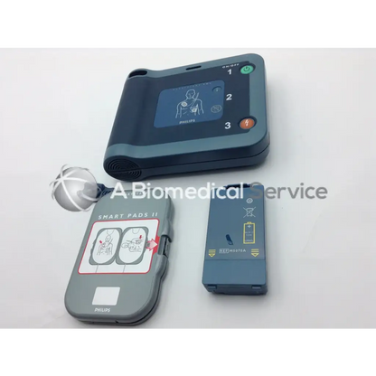 Philips Heartstart FRX AED trainer with gray black casing digital display green orange buttons and Smart Pads II electrodes case