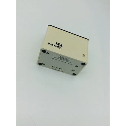 Cream-colored welch allyn model 7235 diagnostic device with black-trimmed top on silver metal welch allyn charging stand 71123