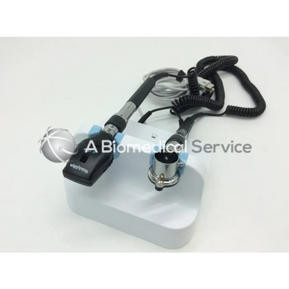 Black and silver handheld welch allyn green series wall transformer ophthalmoscope with coiled cables on white base