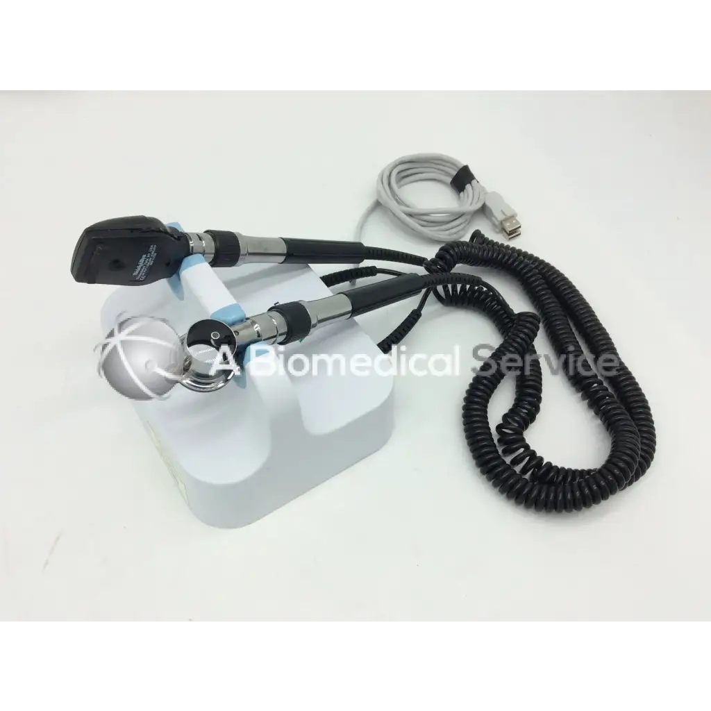 Black and silver welch allyn green series otoscope with coiled cable resting on white stand for wall transformer use